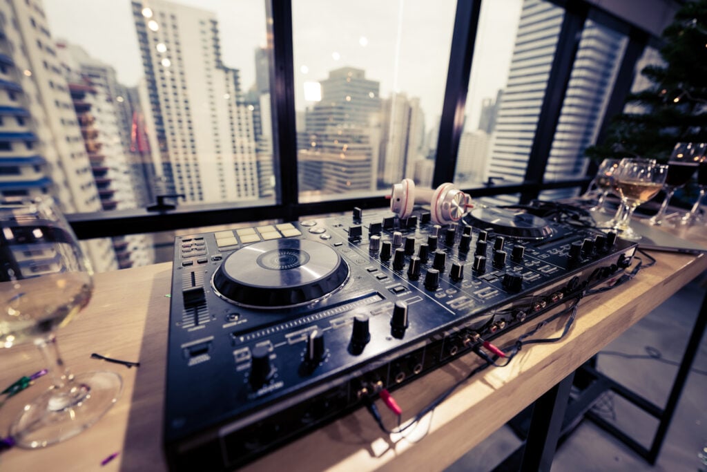 DJ Mixing at Office Party Celebratory Wine Glasses on Table with Urban Cityscape Background.